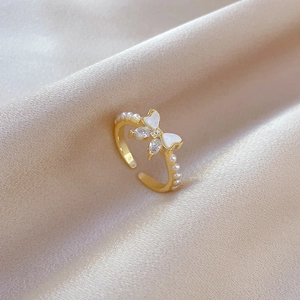 Macro detail of gold butterfly ring with white enamel wings and pearl accents