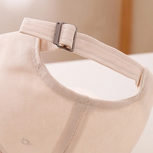 Detail of beige cotton baseball cap featuring adjustable metal buckle and breathable eyelets
