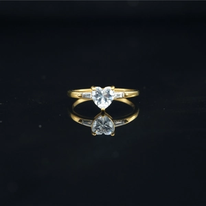 Elegant gold heart-shaped moissanite ring with side stones on black reflective surface