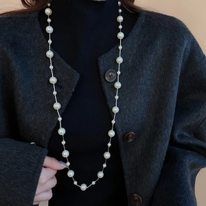 Detail shot of a long pearl necklace with mixed sizes on a model wearing black clothes