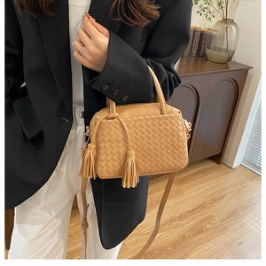 Detail of tan woven leather handbag with double tassel charms worn by a model