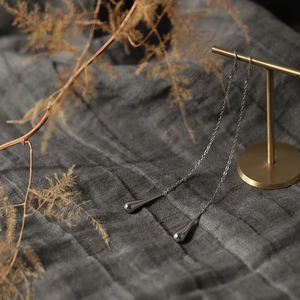 Detailed view of silver teardrop tassel earrings hanging on a minimalist display stand