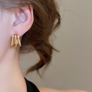 Close-up of golden multi-layer geometric earring on model showing elegant minimalist style