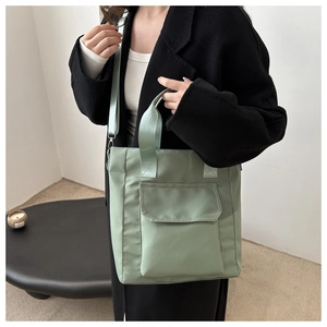 Detail of light green nylon tote bag featuring front pocket and adjustable strap