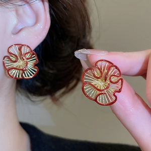 Detailed view of red and gold floral earrings with a glossy enamel finish on earlobes