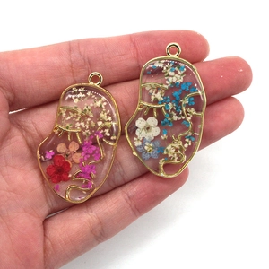Hand holding abstract face resin pendants with colorful dried flowers and gold outlines