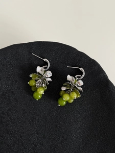 Close-up of C-shaped flower earrings with green crystal grape tassel on black tray