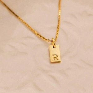 Macro shot of gold square pendant featuring engraved letter R on a brushed metal finish