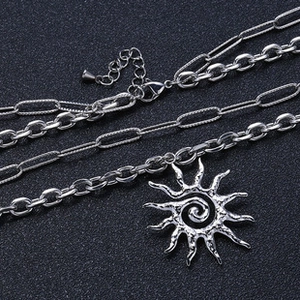 Detail of layered stainless steel necklace with sun pendant and paperclip chain