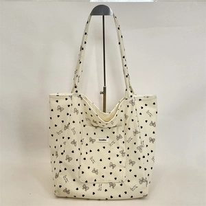 Detail of off-white corduroy tote bag featuring black heart and bow prints with a front pocket