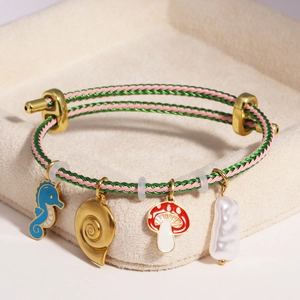Detail of woven bracelet with seahorse, mushroom, conch charms and baroque pearl