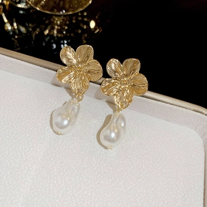 Macro detail of vintage gold flower earring with a baroque white pearl drop on leather