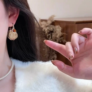 Elegant gold fan-shaped drop earrings with amber stone on model with pearl necklace