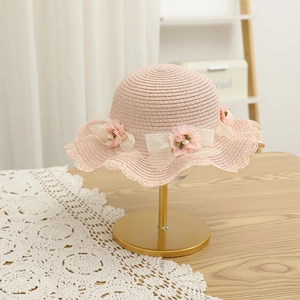 Détail d'un chapeau de paille rose avec nœud en résille et fleurs sur support doré