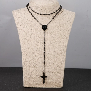 Detailed view of a black rosary necklace with cross pendant and oval holy medal on a bust