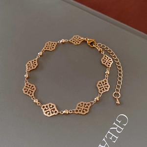 Close-up of a gold clover leaf bracelet with beads and lobster clasp on a dark book
