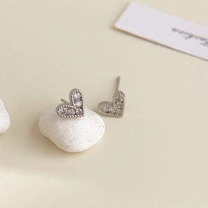 Detail of silver heart earrings with white zircons on white stone background