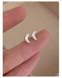 Detailed close-up of mini 925 silver croissant stud earrings held on a fingertip
