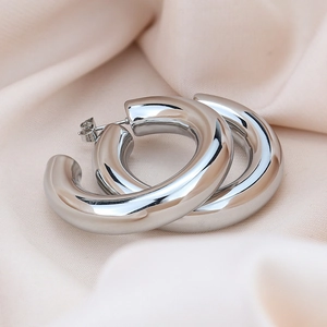 Close-up of chunky silver hollow hoop earrings with polished mirror finish on silk