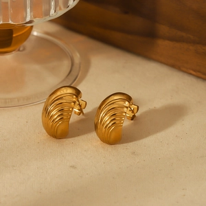 Gros plan de boucles d'oreilles dorées 18k texturées sur tissu et support en bois chic
