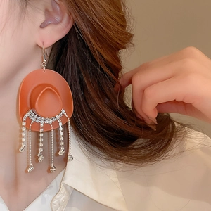 Macro view of cowboy hat earrings with sparkling rhinestone tassels worn by a model