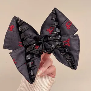 Close-up of black fabric bow hair claw clip with red bunny embroidery detail held in hand