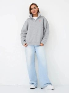 Close-up of grey quarter-zip sweatshirt with red heart embroidery and high-waist denim pants