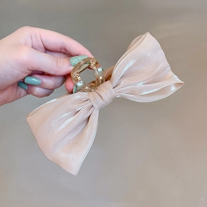 Close-up of champagne satin bow hair claw clip with a transparent grip and metal spring