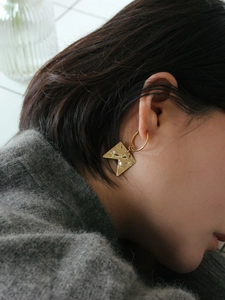 Detailed side view of irregular matte gold earrings with a unique hammered metal texture