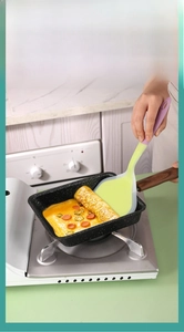Détail de la tête de spatule en silicone vert soulevant des aliments en poêle