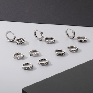 Close-up of silver earrings featuring black zircon, heart motifs, and cross patterns