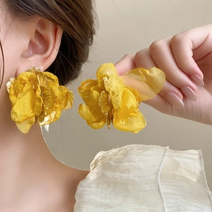 Detailed view of large yellow fabric floral earrings with gold metal centers on a model