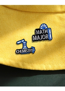 Detailaufnahme von Mathematik- und Chemie-Emaille-Pins auf einer gelben Strickmütze