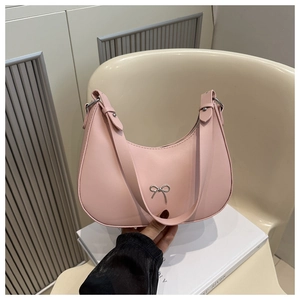 Detail of light pink crescent underarm bag featuring a silver metal bow decoration