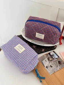 Quilted checkerboard cosmetic bags in red and pink patterns on a minimalist white desk