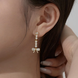 Elegant gold bow earrings with dangling teardrop zircons worn by a model