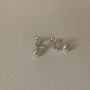 Macro detail of silver stud earrings featuring square zircon and white pearl accents