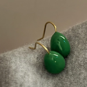 Close-up of green enamel teardrop earrings with elegant gold hooks on grey fabric