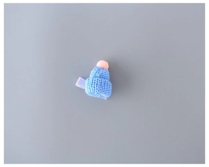 Close-up of blue knitted mini hat hair clip with pink pompom and wool texture