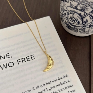 Detail of a golden croissant pendant necklace resting on an elegant cream-colored book