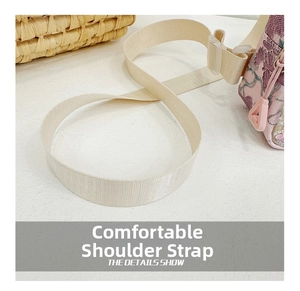 Detail showing the adjustable cream woven shoulder strap and pink floral bag texture