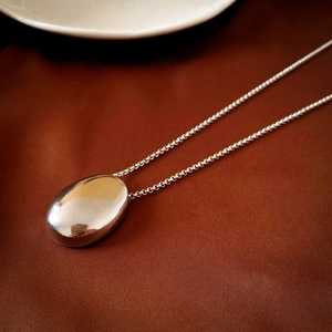 Macro view of a silver bean pendant necklace with smooth polished metallic finish