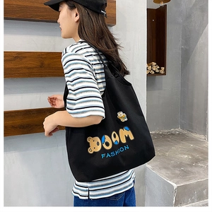 Canvas-Bärentasche mit BOOM FASHION Stickerei, getragen an der Schulter im modernen Interieur