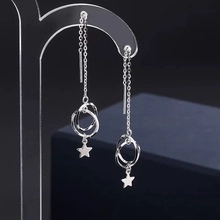 Détail de boucles d'oreilles argentées avec étoiles et anneaux sur support acrylique