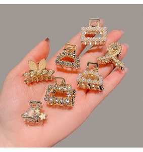 Detail showing seven mini gold hair clips with rhinestones and pearls held in a hand