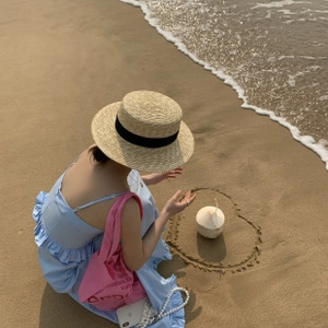 Flat lay of straw hat, blue ruffle dress and pink tote bag on a summer beach background