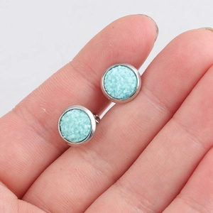 Close-up of 8mm light blue glitter texture stud earrings with silver base held by hand