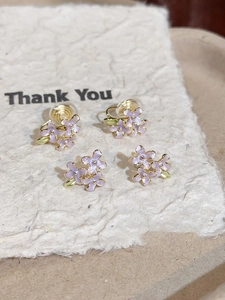 Macro detail of lilac enamel flower earrings with gold finish on a decorative card
