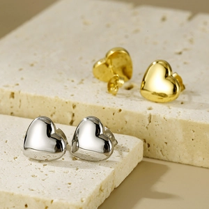 Polished gold and silver heart earrings displayed on textured natural beige stone