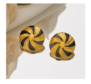 Detail view of round gold and black swirl enamel earrings on a reflective surface